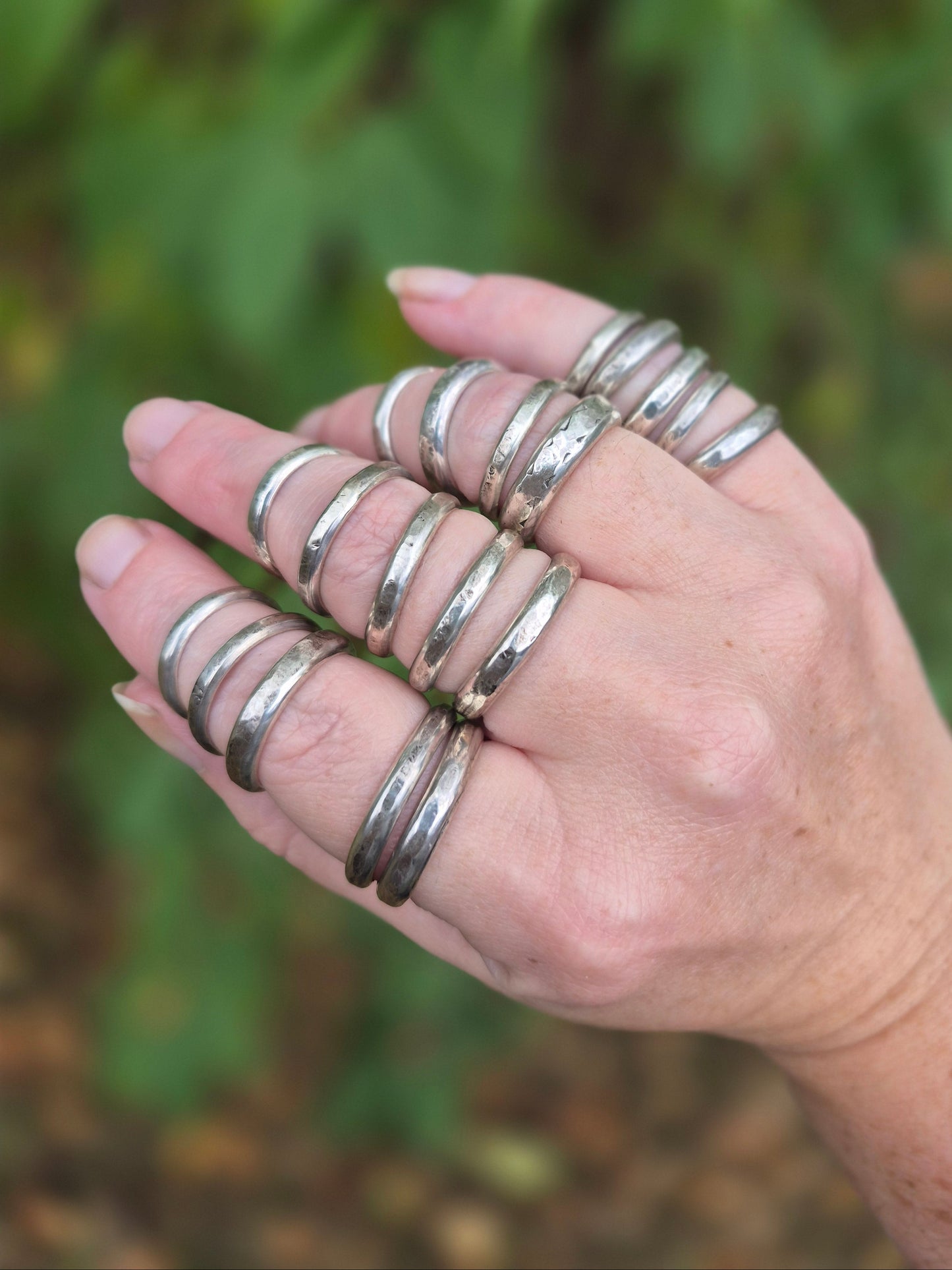 Hand wearing multiple silver rings with a blurred green background