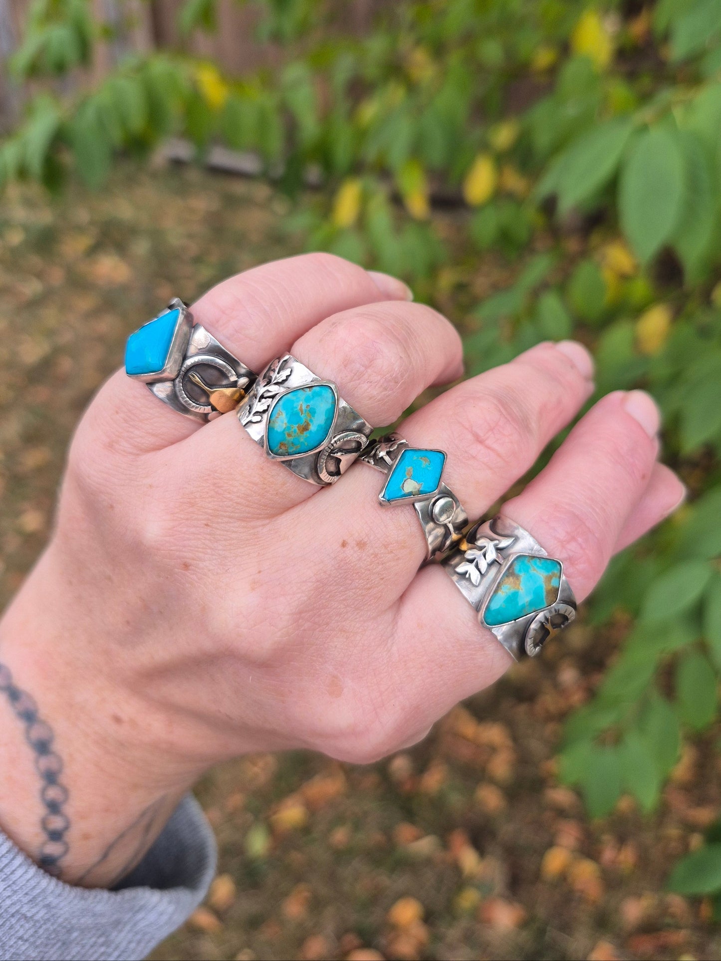 Hand wearing multiple silver and turquoise rings with a blurred natural background
