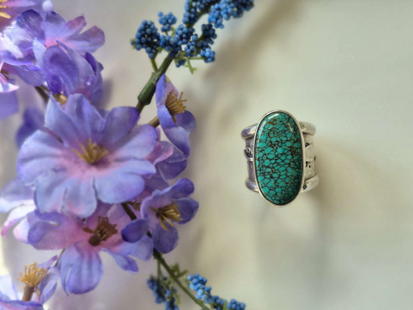 Silver ring with turquoise stone next to purple flowers