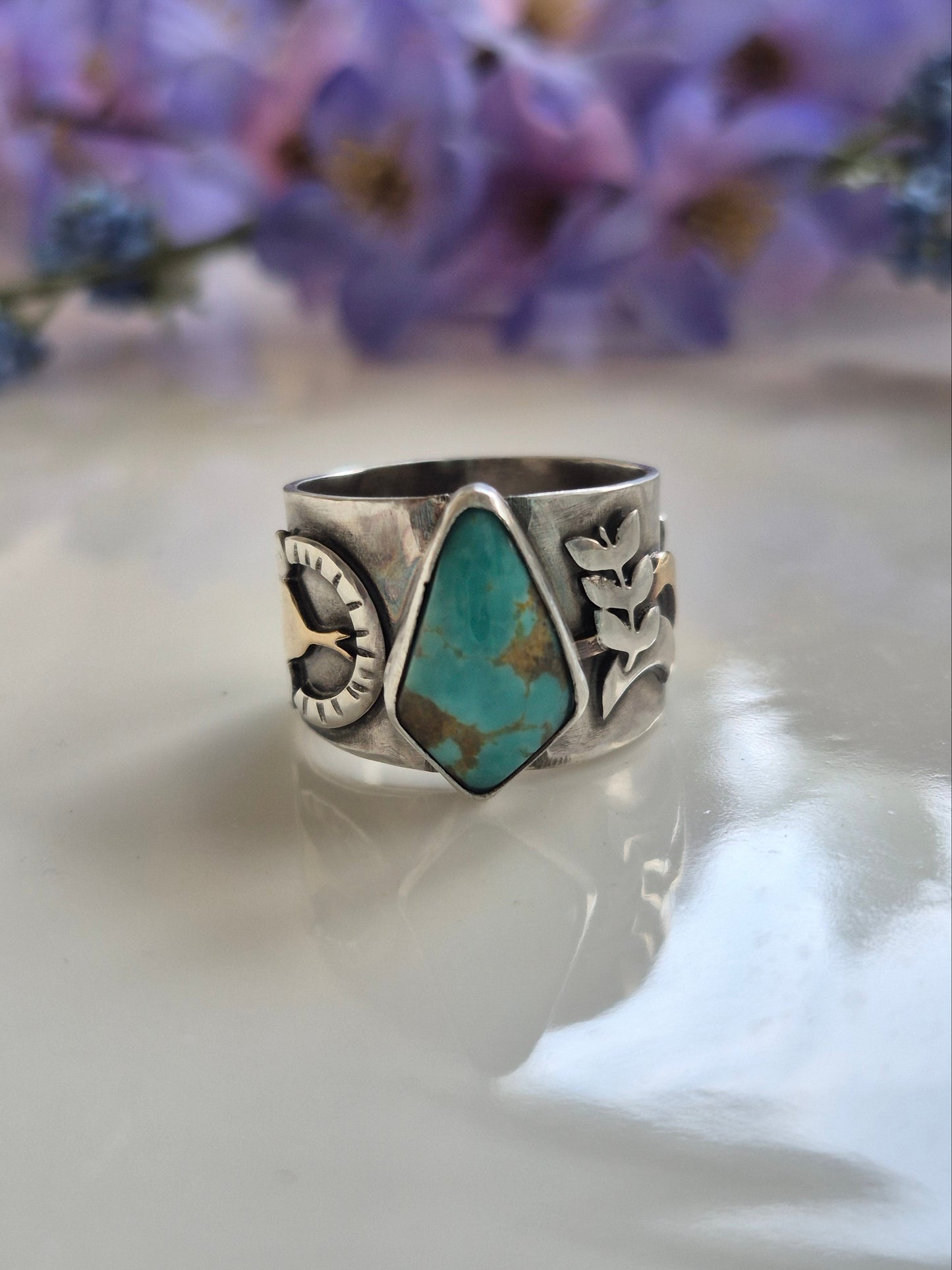 Silver ring with turquoise stone on a white background with purple flowers