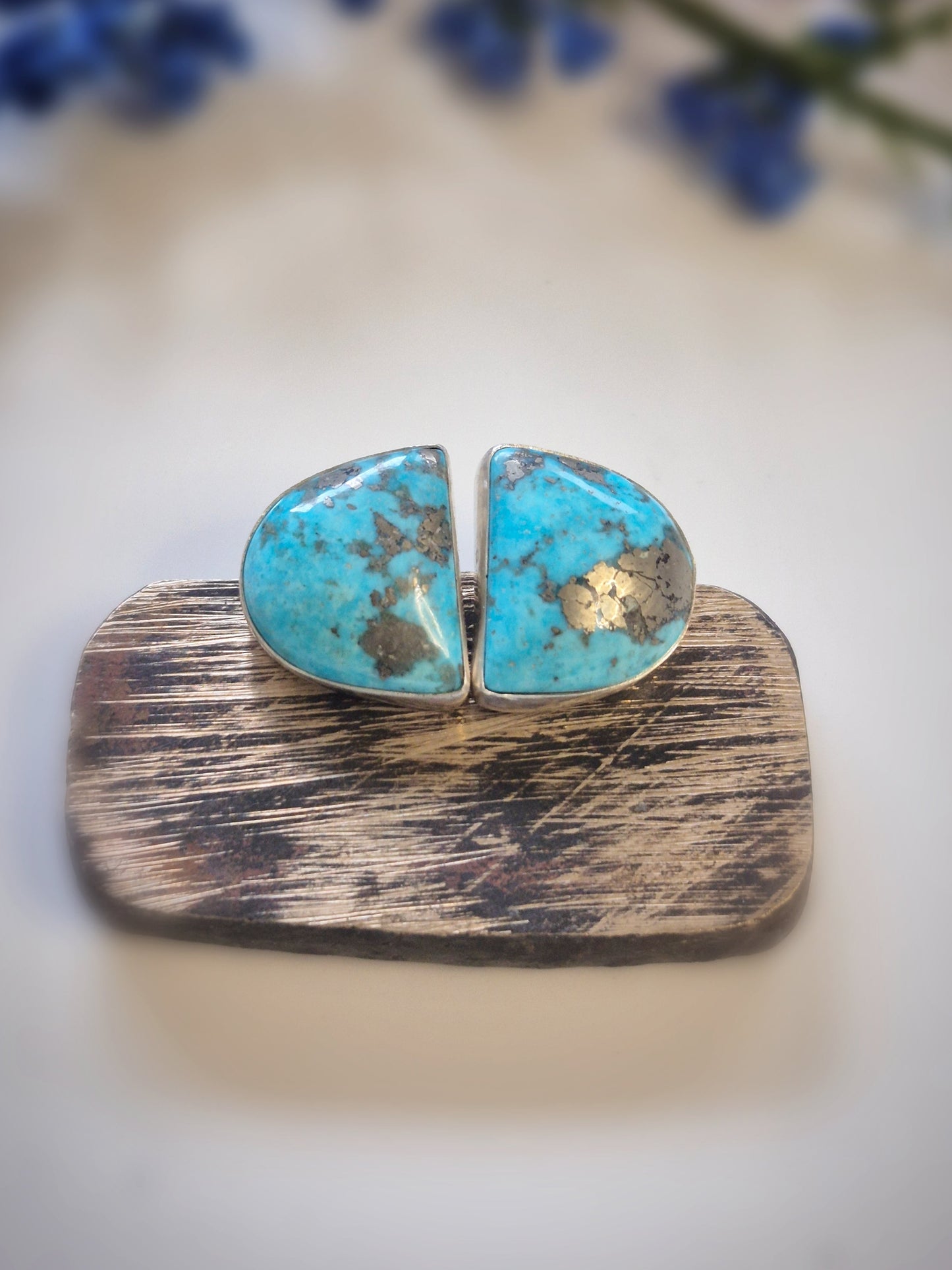 Turquoise earrings on a wooden stand with a blurred floral background