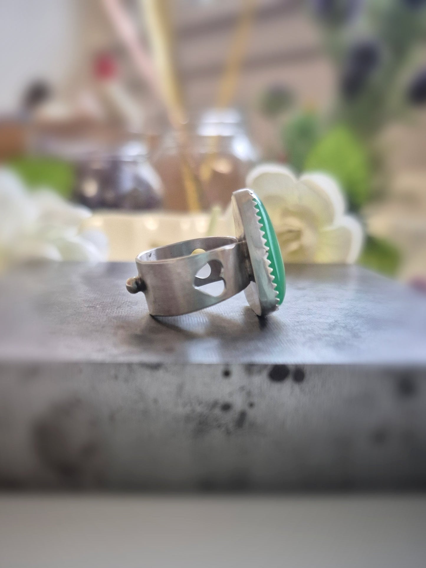 Silver ring with green gemstone on a marble surface with blurred background