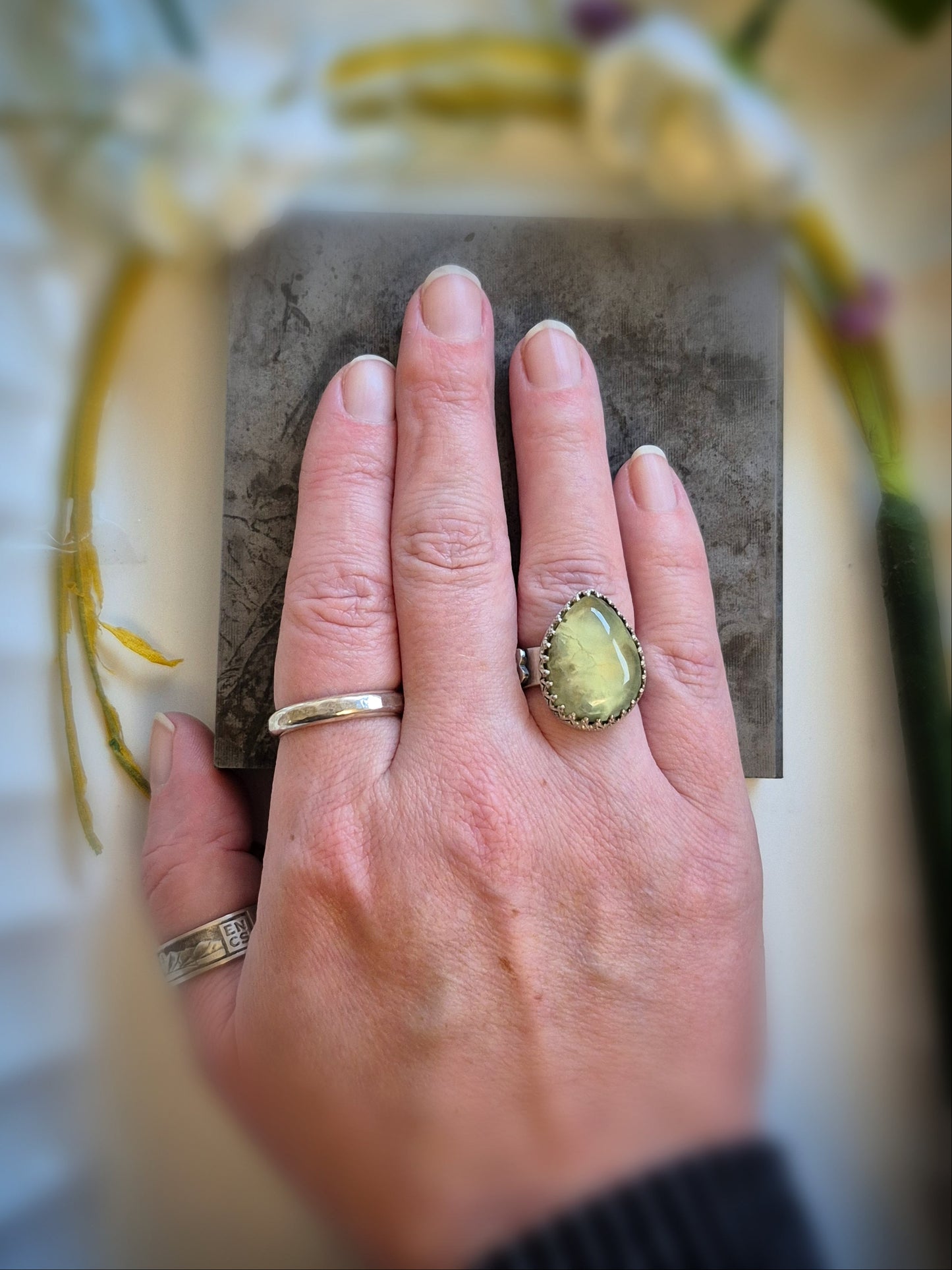 Hand wearing a ring with a yellow prehnite gemstone on a neutral background
