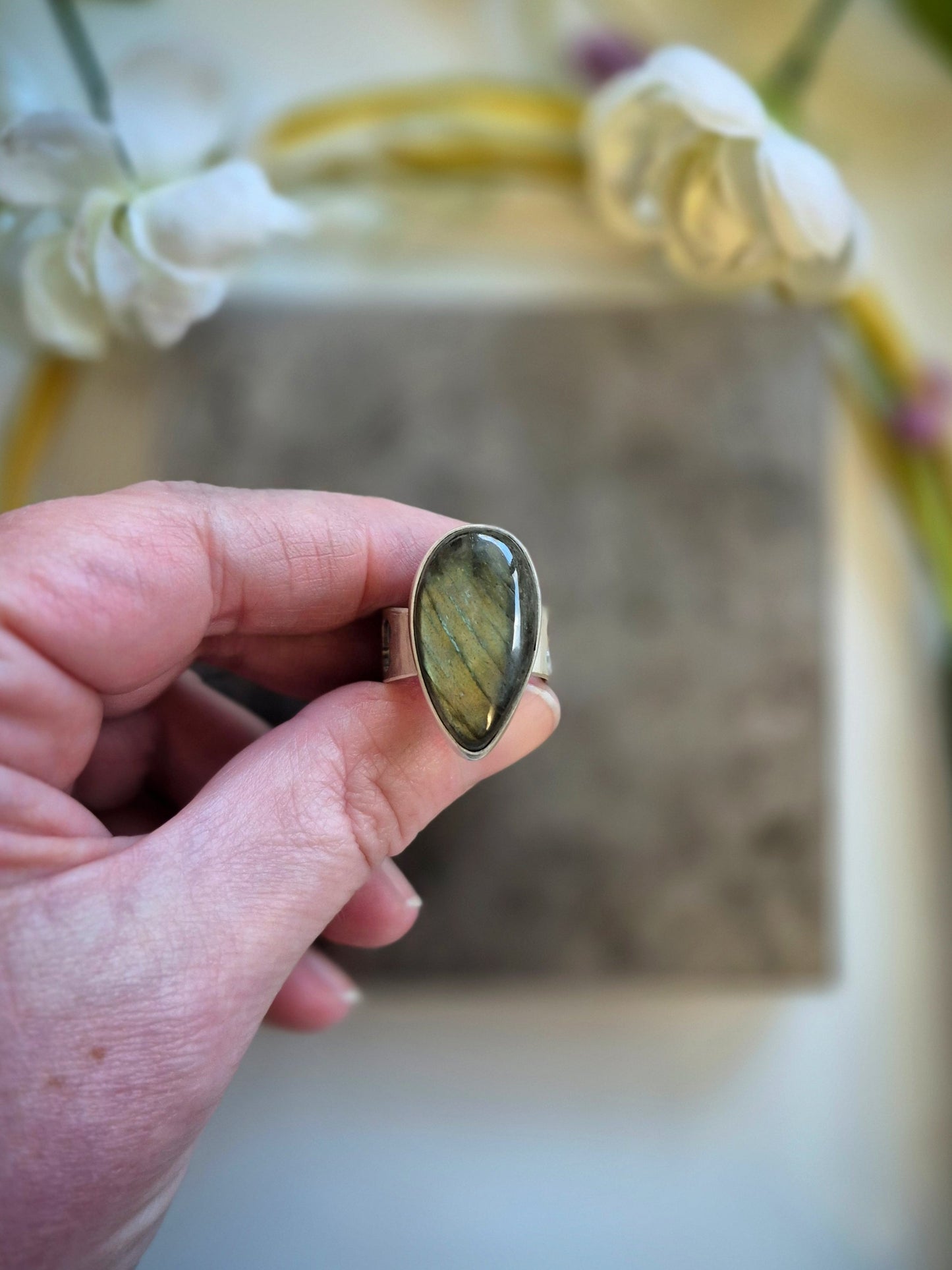 Hand holding a ring with a green labradorite stone against a blurred background