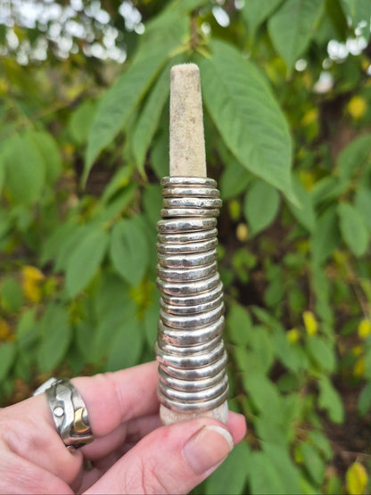 Hand holding a ring holder with multiple silver stacker rings against a green leafy background
