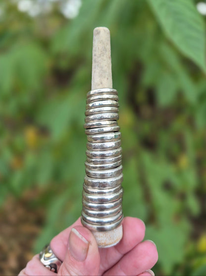Hand holding a ring holder with several silver rings against a blurred natural background