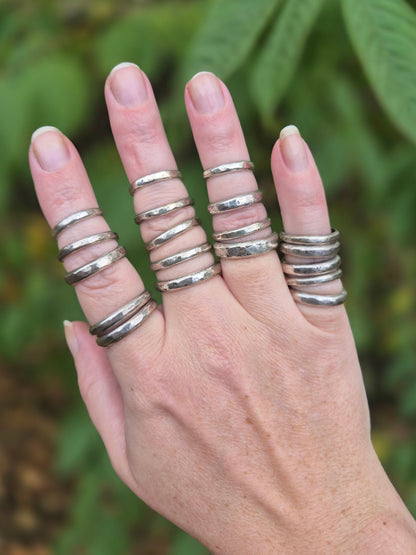 Hand wearing multiple silver stacking rings with a blurred green background