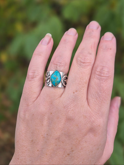 Hand wearing a silver ring with a turquoise stone against a blurred green background