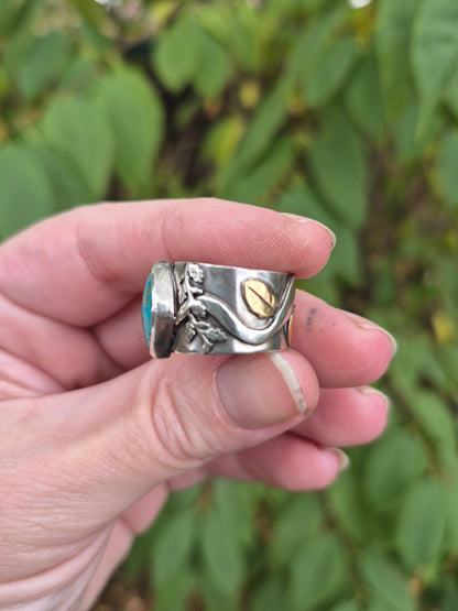 Hand holding a silver ring with a tuquoise stone against a blurred green background