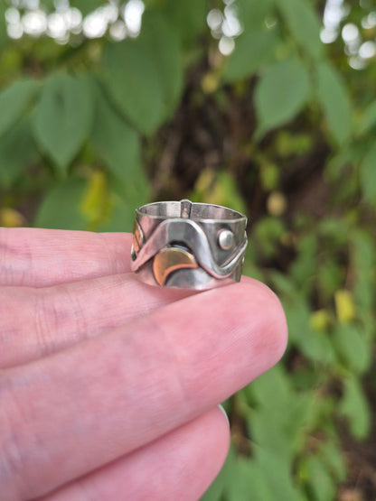 Silver ring held in a hand with a blurred green leafy background