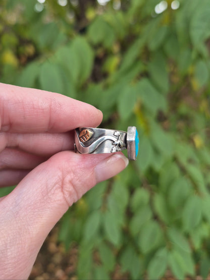 Silver ring with a turquoise stone held between fingers against a blurred green leafy background