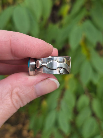 Hand holding a small silver ring with a blurred green leafy background
