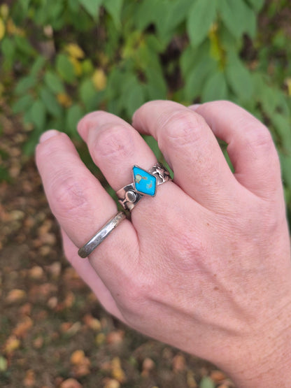 Hand wearing a silver ring with a tuquoise gemstone against a natural background