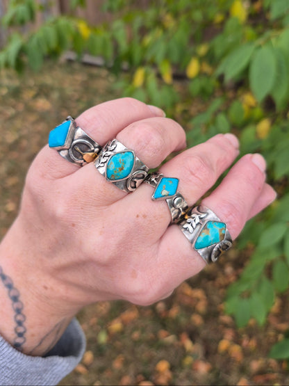 Hand wearing multiple silver and turquoise rings with a blurred natural background