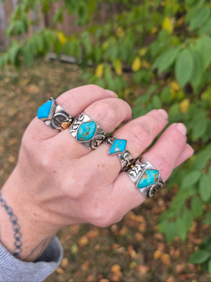 Hand wearing multiple silver and turquoise rings with a blurred natural background