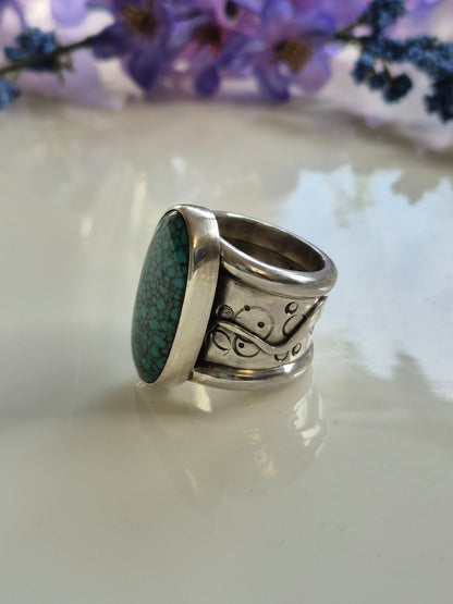 Silver ring with turquoise stone on a white surface with purple flowers in the background