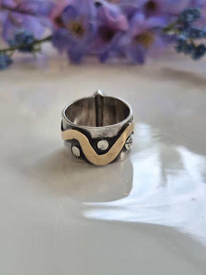Silver ring with decorative brass snake design on a white surface with flowers in the background