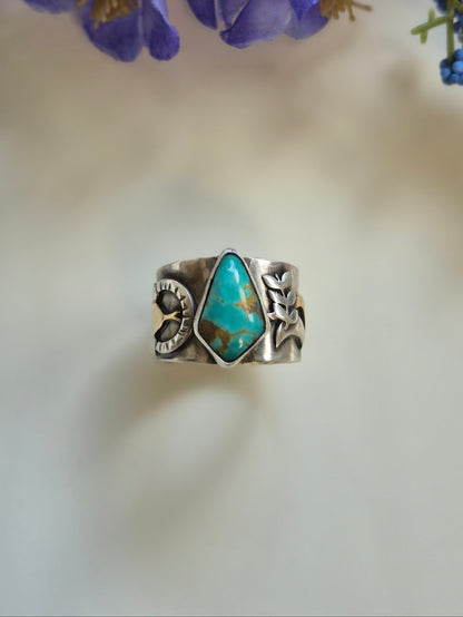 Silver ring with turquoise stone next to purple flowers on a blurred background
