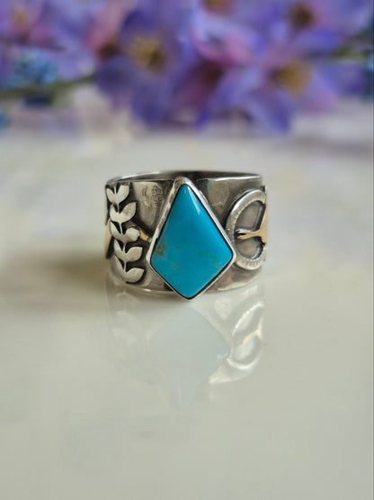 Silver ring with turquoise stone on a white background with blurred purple flowers.