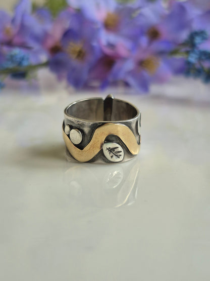 Silver ring with a brass snake symbol next to purple flowers