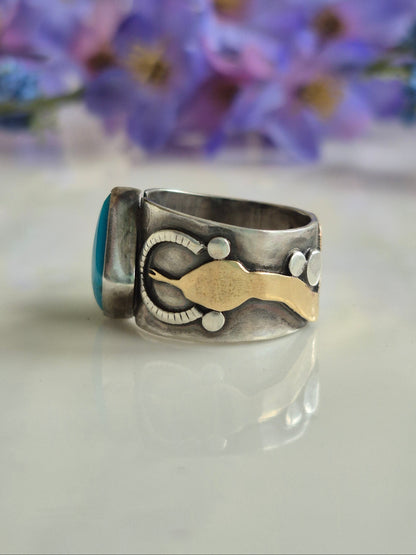 Silver ring with a gold-coloured brass snakehead accent on a white background with blurred purple flowers.
