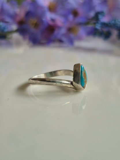 Silver ring with a tuquoise stone on a white surface with a floral background