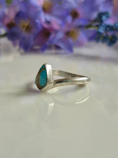 Silver ring with a turquoise stone on a white background with purple flowers.