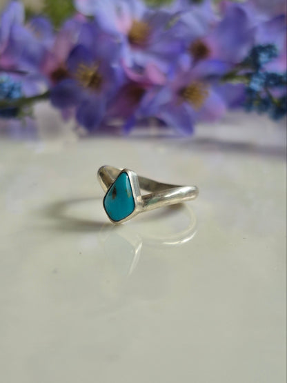 Silver ring with a tuquoise stone on a white surface with purple flowers in the background