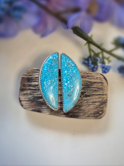 Turquoise gemstone earrings and wooden band against a blurred floral background