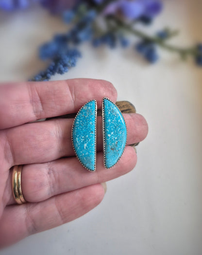 Turquoise earrings held between fingers with a blurred floral background