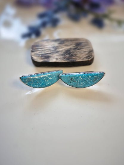 Turquoise earrings with gold speckles on a light background