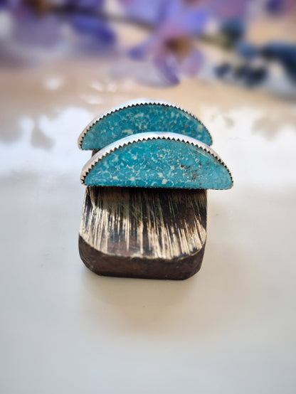 Turquoise earrings with wooden base on a white surface