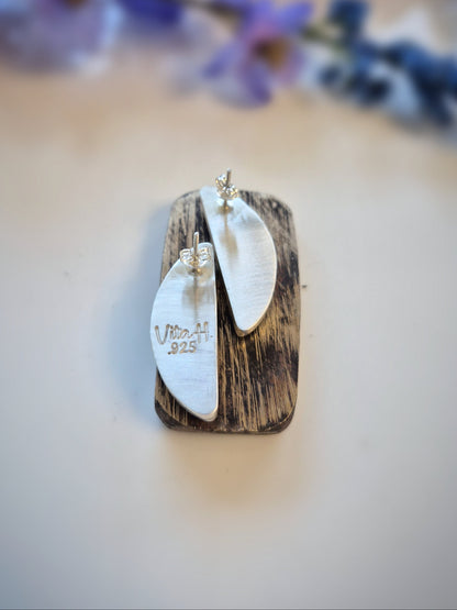 Pair of silver earrings on a wooden block with a blurred floral background