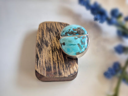 Turquoise gemstone earrings on a wooden stand with blurred purple flowers in the background