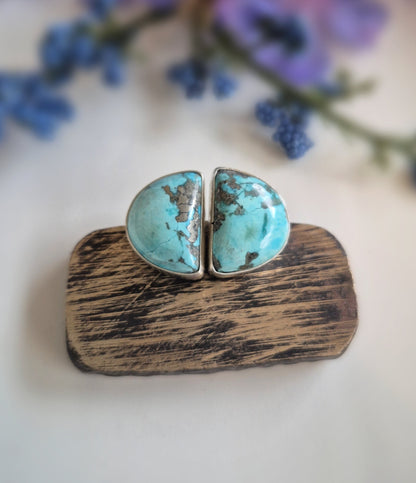 Turquoise stone earrings on a wooden block with purple flowers in the background