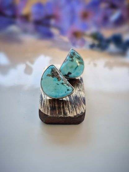 Turquoise earrings on a wooden stand with a blurred floral background