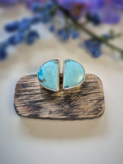 Turquoise stone earrings on a wooden base with blurred flowers in the background