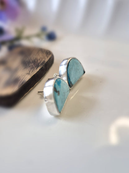 Turquoise stone stud earrings on a light surface with a blurred background