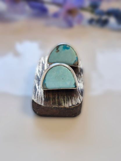 Turquoise stone ring on a wooden stand with a blurred floral background