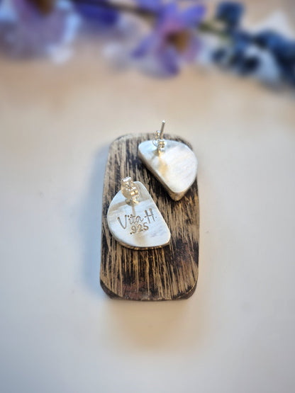 Two crescent-shaped earrings on a wooden surface with blurred flowers in the background