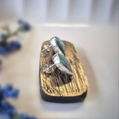 Silver earrings on a wooden stand with blurred blue flowers in the background