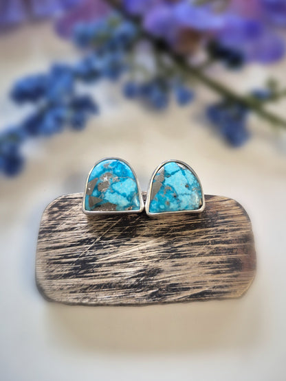 Turquoise stone earrings on a wooden stand with blurred purple flowers in the background