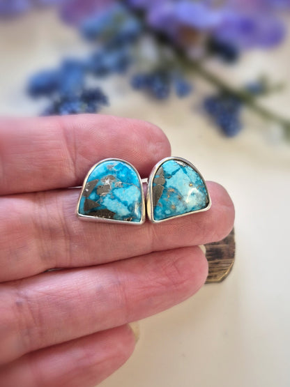 Turquoise earrings held between fingers with a blurred floral background