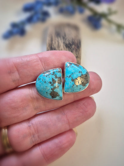 Turquoise earrings held between fingers with a blurred natural background