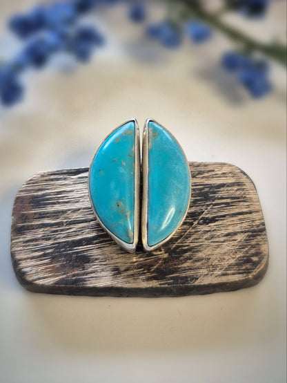 Jewelry with turquoise stones and wooden base against a blurred floral background