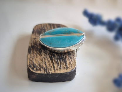 Turquoise gemstone earrings on a wooden base, with blurred blue flowers in the background.