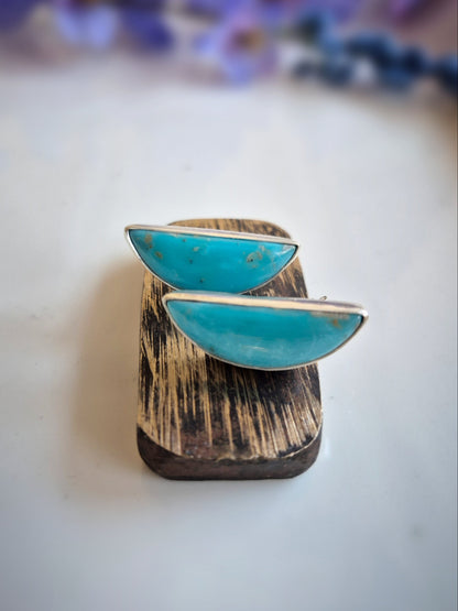 Turquoise gemstone earrings on a wooden stand with a blurred floral background