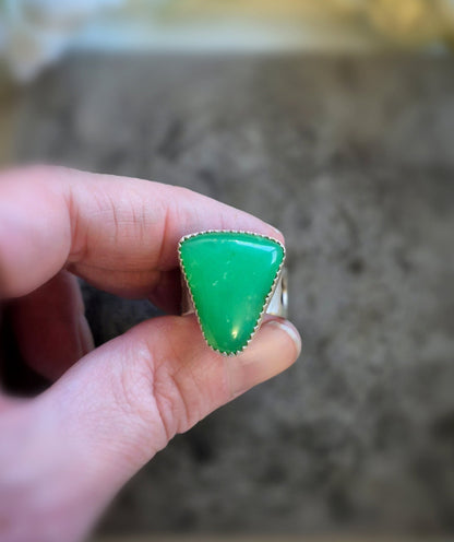 Green triangular chrysoprase gemstone ring held by a hand with a blurred background