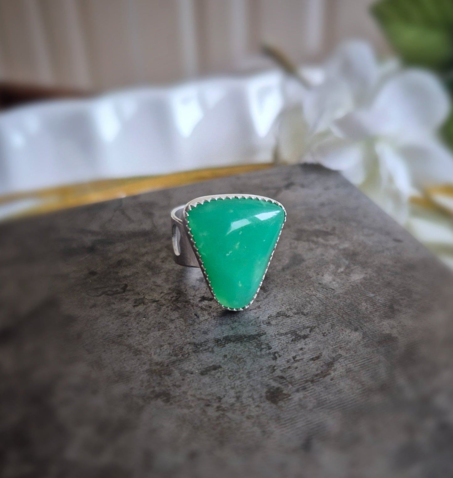 Green triangular chrysoprase gemstone ring on a dark surface with a blurred background
