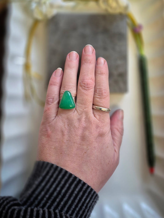 Hand wearing a green triangular chrysoprase ring with a blurred background